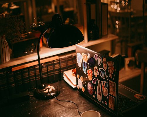 person adjusting desk lamp over a laptop in a cozy home office
